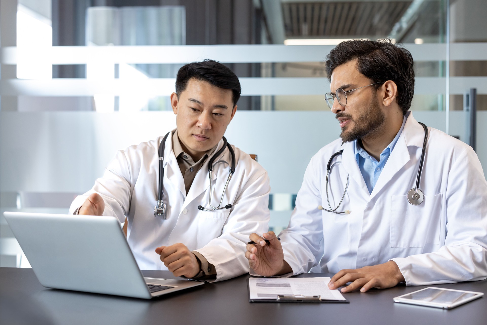 Doctors collaborating in modern office, discussing patient case on laptop, teamwork in healthcare setting